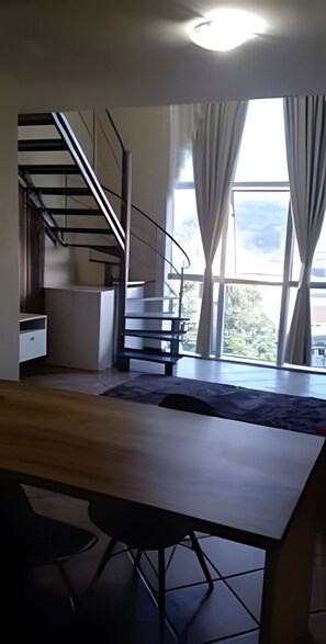 A modern room with a wooden desk, a spiral staircase, and large windows with curtains.