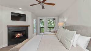 Ein Schlafzimmer mit Kamin, einem großen Bett, Deckenventilator und Blick ins Freie.
