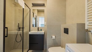 A modern bathroom with a glass shower enclosure, a white sink, a dark cabinet, and a toilet. - ShortStayPoland Zdziechowskiego B151 (Warsaw)