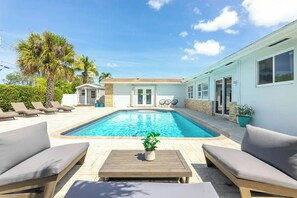 A pool area with lounge chairs, a wooden table, and a small building with a door. - 5-bed Villa with Pool, minutes to Hard Rock hotel and Beach (Hollywood)