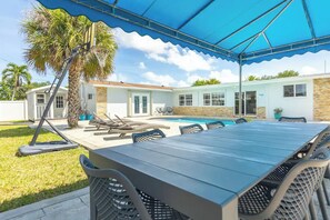 A covered outdoor area with a pool, a dining table, and lounge chairs.