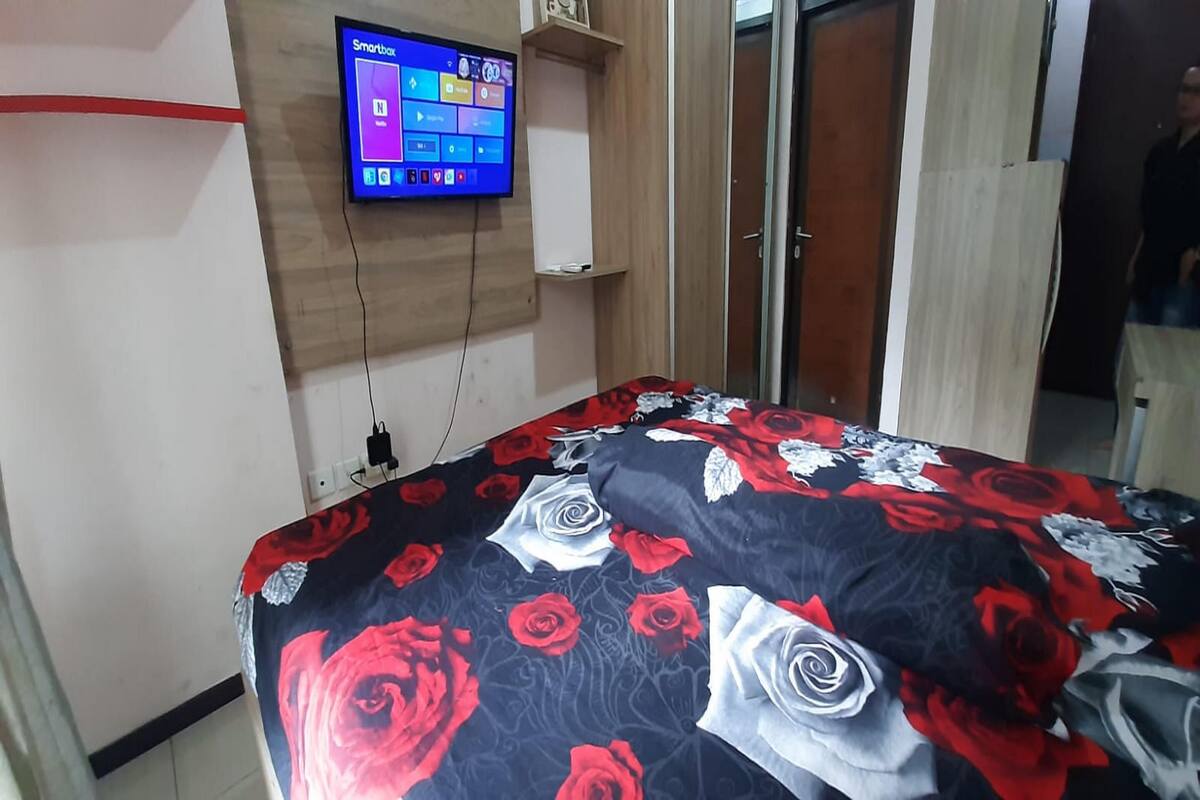 Une chambre à coucher avec un lit recouvert d’une couvre-lit à motifs floraux, un téléviseur fixé au mur et une armoire.