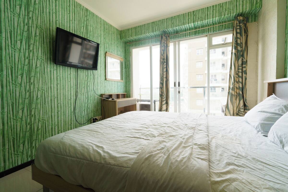Une chambre d’hôtel avec un lit, un téléviseur fixé au mur, un petit bureau et une fenêtre donnant sur des immeubles.