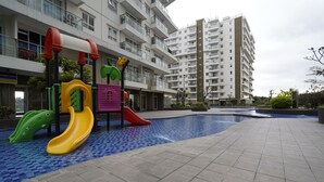 Zona de juegos infantiles con toboganes y estructuras para escalar, rodeada por una piscina y edificios residenciales.