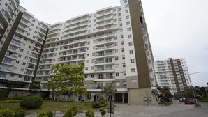 Un edificio residencial alto con varios balcones, un patio ajardinado y una zona de estacionamiento.