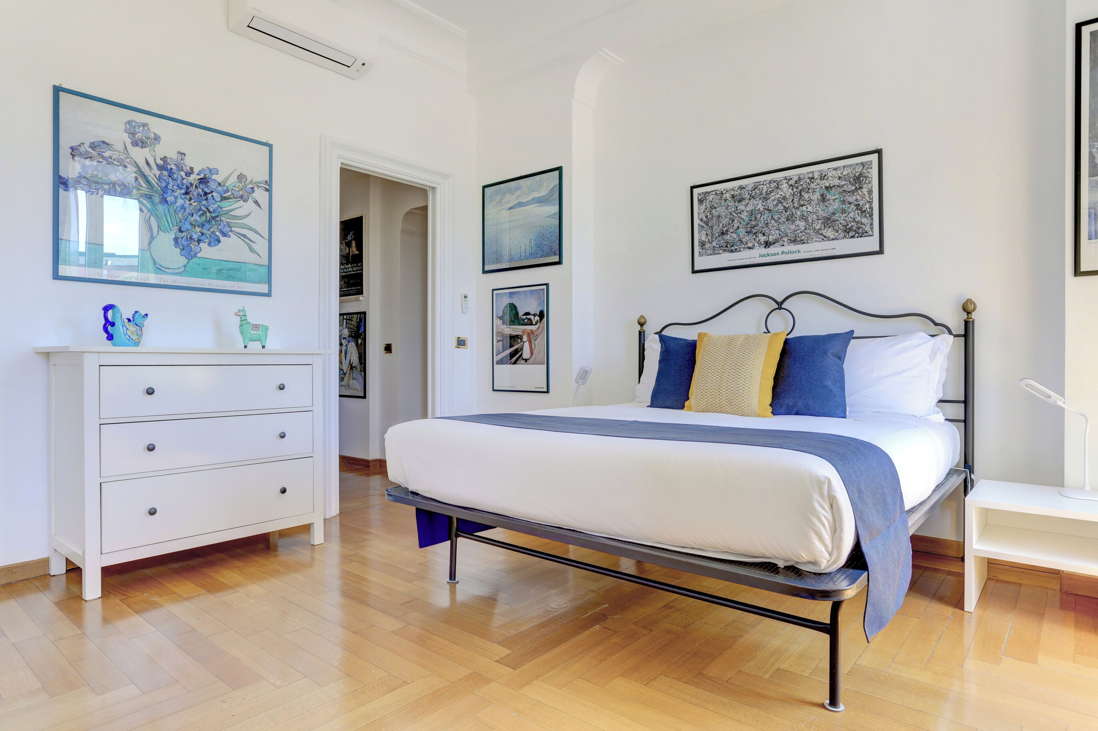Une chambre à coucher avec un lit, une commode et une table de chevet. Des tableaux encadrés ornent les murs.