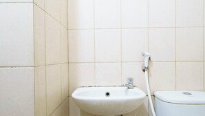 A bathroom with a white sink, a toilet, and a shower hose. - OYO 93945 The Suite Metro Apartemen By Sa (Bandung)