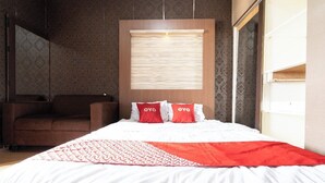 A hotel room with a large bed, two red pillows with 'OYO' branding, a wooden headboard, and a patterned wall. - OYO 93945 The Suite Metro Apartemen By Sa (Bandung)