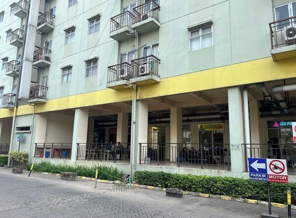 A multi-story building with balconies, a covered entrance, and a sign indicating a motor vehicle parking area. - OYO 93945 The Suite Metro Apartemen By Sa (Bandung)