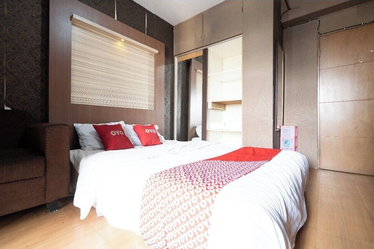 A hotel room with a bed, a sofa, a large window with blinds, and a wardrobe.