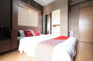 A hotel room with a bed, a sofa, a large window with blinds, and a wardrobe. - OYO 93945 The Suite Metro Apartemen By Sa (Bandung)