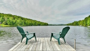 A wooden dock with two green Adirondack chairs facing a calm lake surrounded by forested hills. - Bord de lac | Chalet du Bonheur (Amherst)