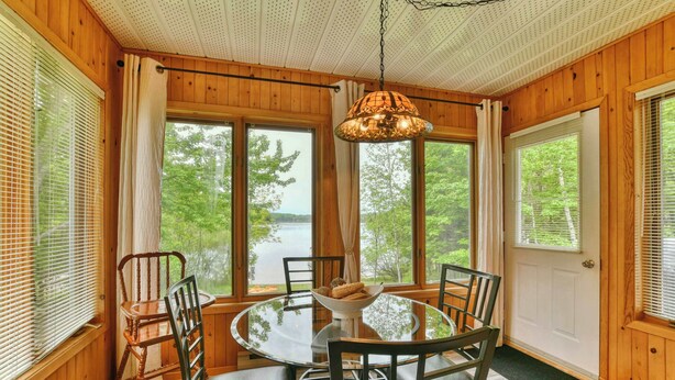 A wooden cabin with a round dining table, chairs, and a hanging light fixture. - Bord de lac | Chalet du Bonheur (Amherst)