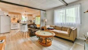 A spacious living area with a sofa, a coffee table, and a kitchen in the background. - Bord de lac | Chalet du Bonheur (Amherst)