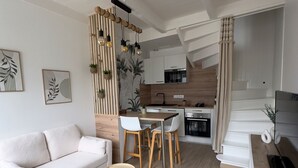 A modern living room with a sofa, two small round tables, and a dining area with stools. - La Petite M (Tréméreuc)
