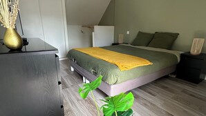 A modern bedroom with a sloped ceiling, a bed with green and yellow bedding, a bedside table, and a large green plant in the foreground. - La Petite M (Tréméreuc)