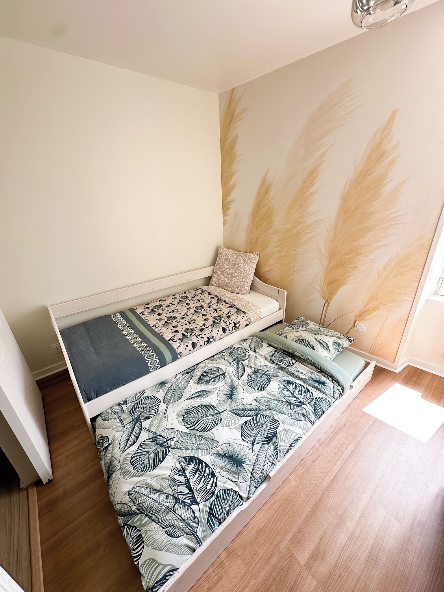 Et kompakt værelse med to senge, trægulv, vægmonteret seng og stort vindue.