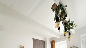 A modern living room with a wooden dining table, white chairs, a flat-screen TV, and decorative plants. - La Petite M (Tréméreuc)