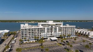 A multi-story hotel with balconies, a parking lot, and a view of the water.