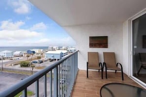 A balcony with two chairs, a glass table, and a view of the sea and buildings.
