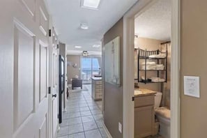 A hallway with a tiled floor, a door, a small kitchen area with a sink and counter, and a view of a balcony.