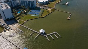 Vista aérea de una propiedad frente al mar con cancha de tenis, muelle y edificios colindantes.