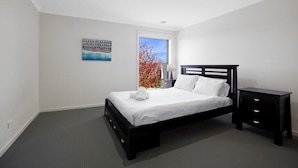 Een slaapkamer met een bed, nachtkastjes, een raam en een schilderij aan de muur.