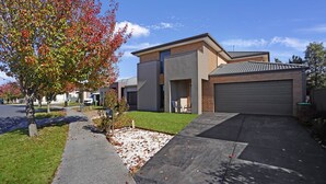 Een modern huis met twee verdiepingen, een garage, een verzorgd gazon en een boom met herfstbladeren.