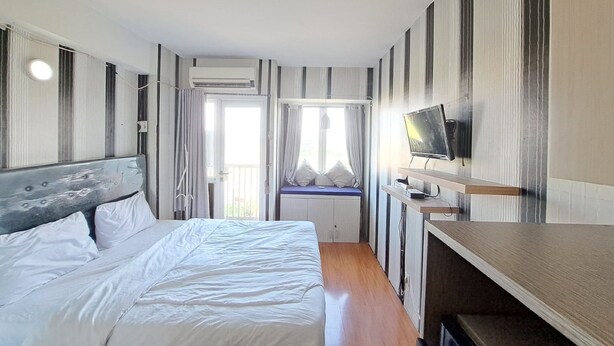 A modern hotel room with a large bed, a TV on a wooden shelf, and a window with curtains. - Capital O 93961 Apartement Sentraland By Helen (Karawang)