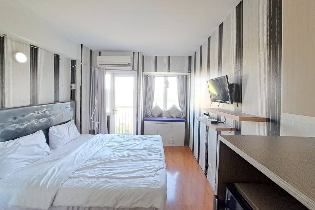Una habitación de hotel moderna con una cama grande, un televisor sobre una estantería de madera y una ventana con cortinas.