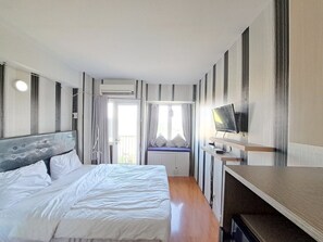A modern hotel room with a large bed, a TV on a wooden shelf, and a window with curtains.