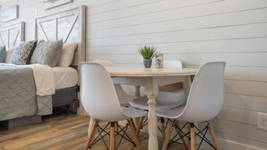Una habitación acogedora con una cama, una mesa de comedor con sillas, un reloj y una pared con líneas horizontales.