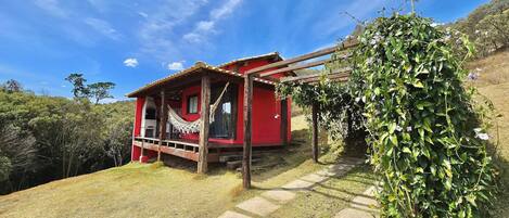 A red building with a porch and a hammock, surrounded by greenery and a clear sky.