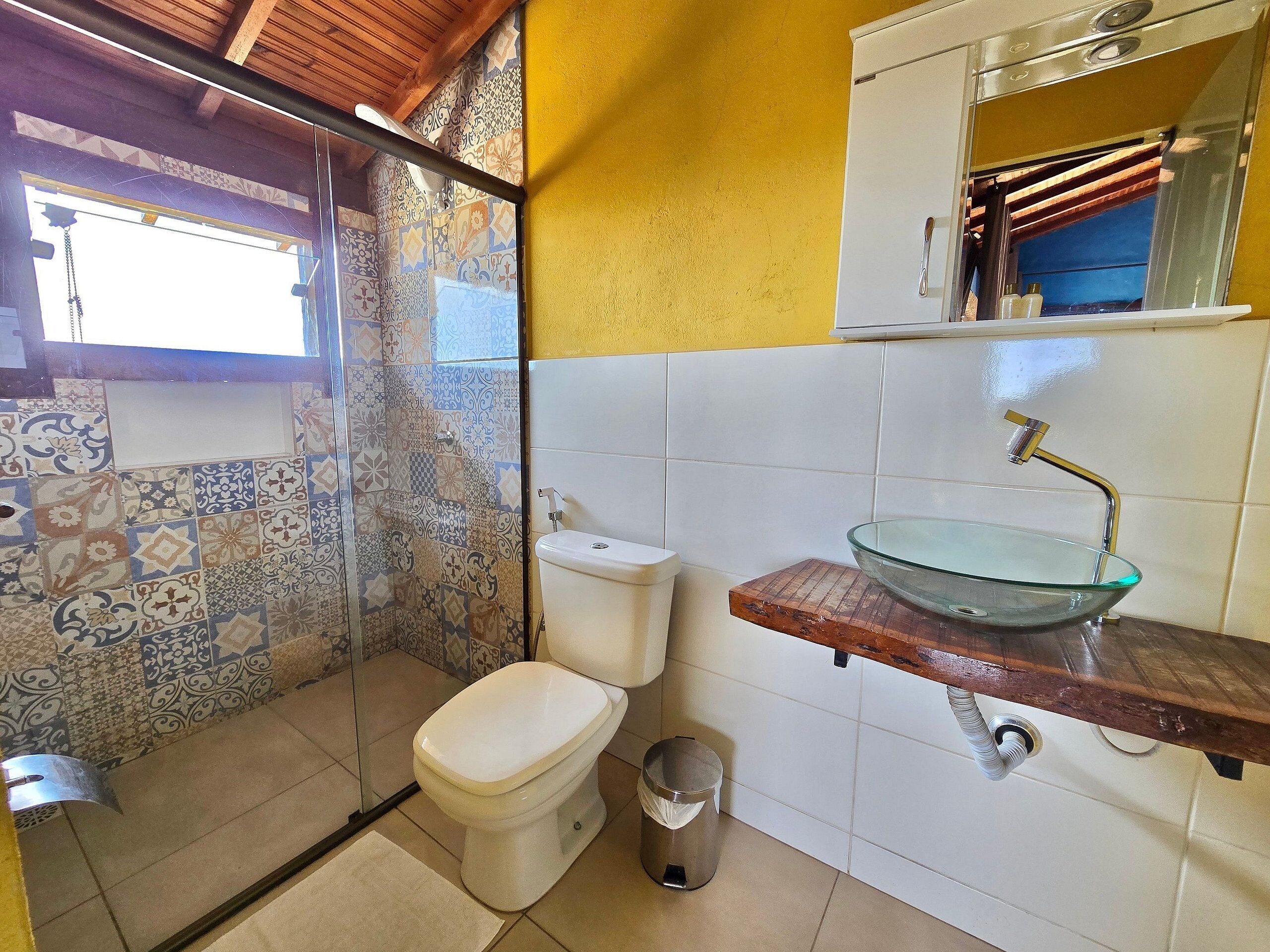 A bathroom with a glass sink, toilet, and shower area.