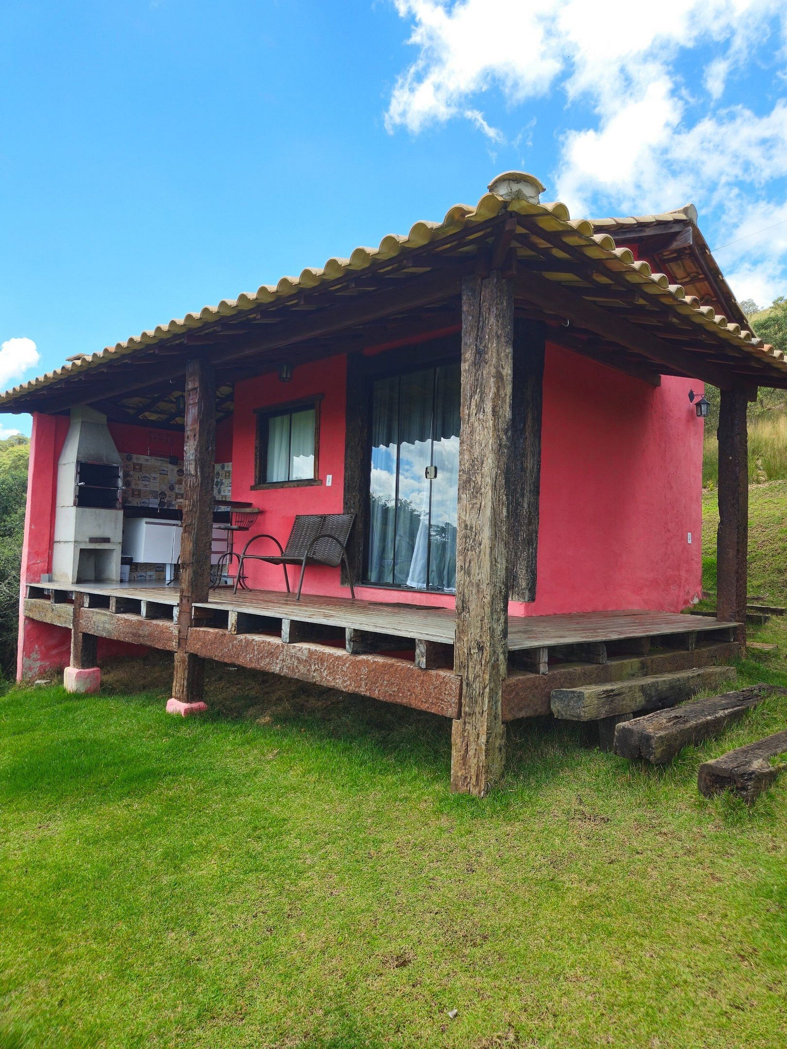 A small, red-roofed building with a patio area, a grill, and a chair.