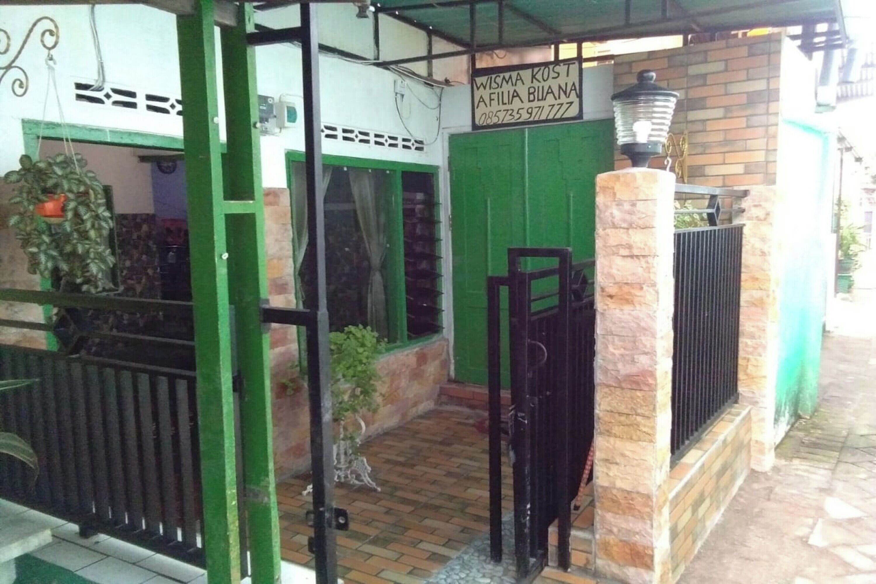 Una entrada con portón, una puerta verde, un cartel sobre la puerta y una planta en maceta a la izquierda.