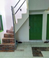 Una escalera conduce a una puerta verde, una ventana pequeña y un suelo de baldosas con un diseño decorativo.