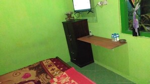 A room with a green wall, a wooden cabinet, a small shelf with bottles, a bed with a patterned bedspread, and a window with curtains. - Hotel O Wisma Kost & Penginapan Afilia Buana Syariah (Tulungagung)