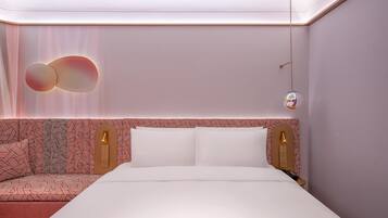 A modern hotel room with a neatly made bed, a patterned headboard, and a wall-mounted light fixture.