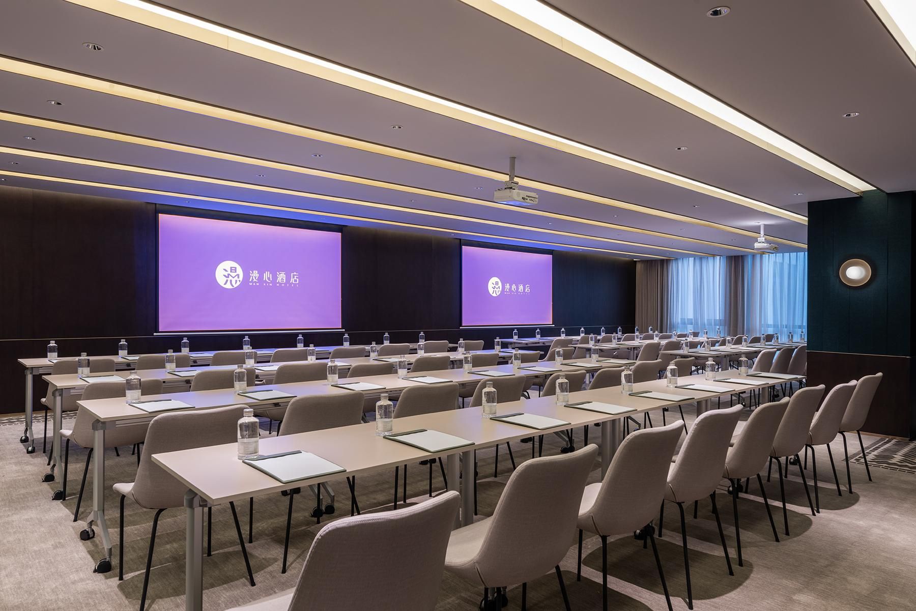 A conference room with rows of tables and chairs, a large screen, and a projector.