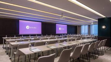 A conference room with rows of tables and chairs, a large screen, and a projector.