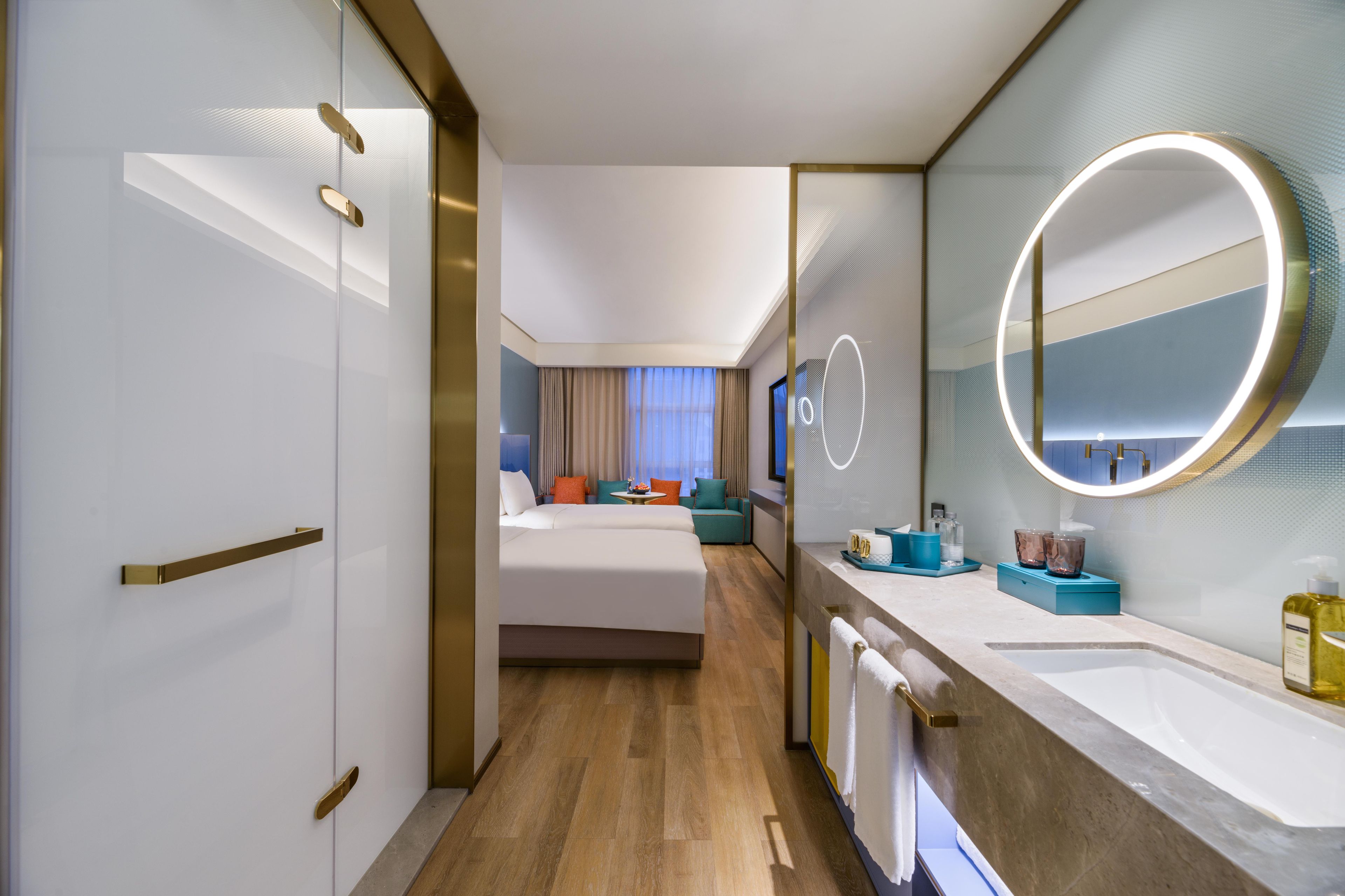 A hotel room with a large bed, a bathroom with a mirror and sink, and a view of the hotel lobby.