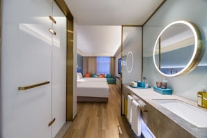 Une chambre d’hôtel avec un grand lit, une salle de bain avec un miroir et un lavabo, et une vue sur le hall de l’hôtel.