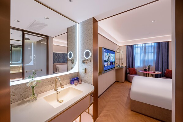A hotel room with a large mirror, a sink, a television, a bed, and a small table with a chair. - Manxin Hotel Yantai Binhai Plaza (Yantai)