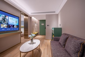 Eine moderne Hotelhalle mit einem Flachbildfernseher, einem runden Tisch mit einer Vase, einer Couch und einer grünen Tür im Hintergrund.