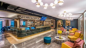 A modern bar area with a marble countertop, seating with yellow and pink chairs, and a blue ottoman. - Manxin Hotel Yantai Binhai Plaza (Yantai)