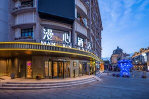 A hotel with a curved entrance, a sign in a foreign language, and a traditional building in the background. - Manxin Hotel Yantai Binhai Plaza (Yantai)