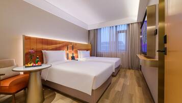 Una habitación de hotel con cama, escritorio, silla, televisor y ventana con cortinas.