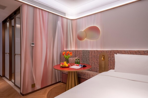 A hotel room with a bed, a small round table with a fruit bowl, a vase with flowers, and a patterned headboard. - Manxin Hotel Yantai Binhai Plaza (Yantai)