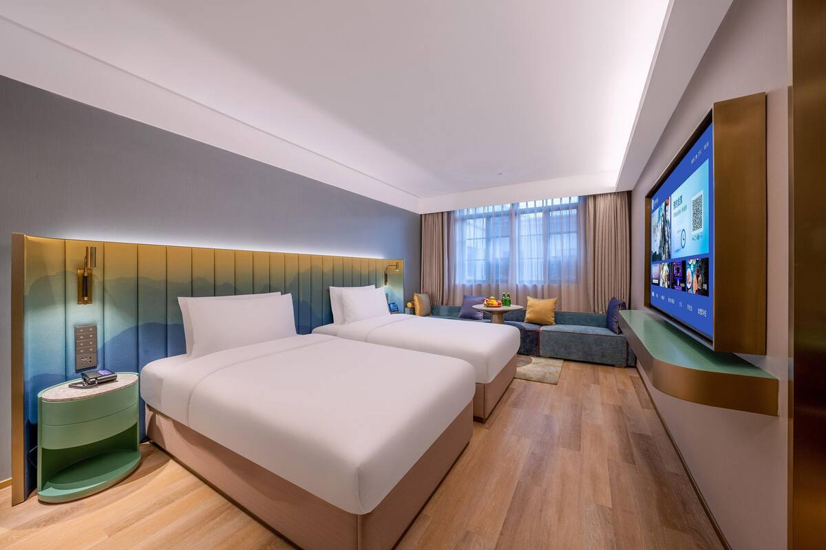 Ein Hotelzimmer mit zwei Betten, einem Fernseher, einem kleinen Tisch mit Obstschale und einem Sofa.